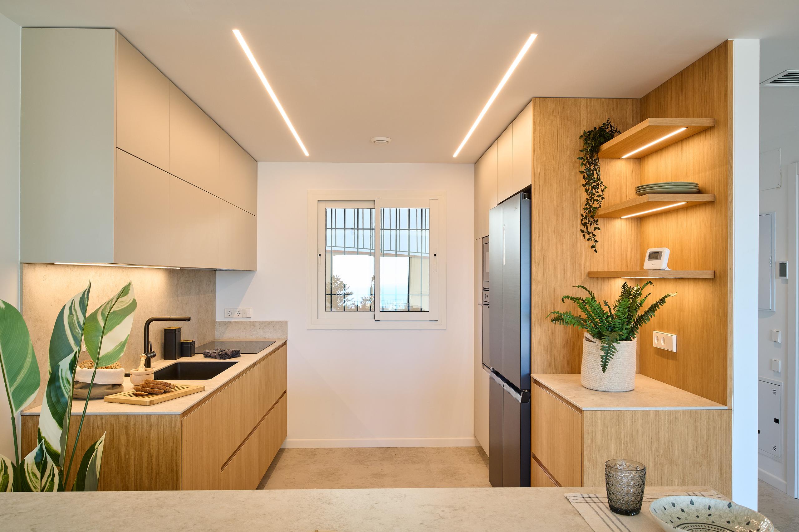 Cocina moderna con mobiliario de madera clara, encimeras de piedra, estanterías iluminadas