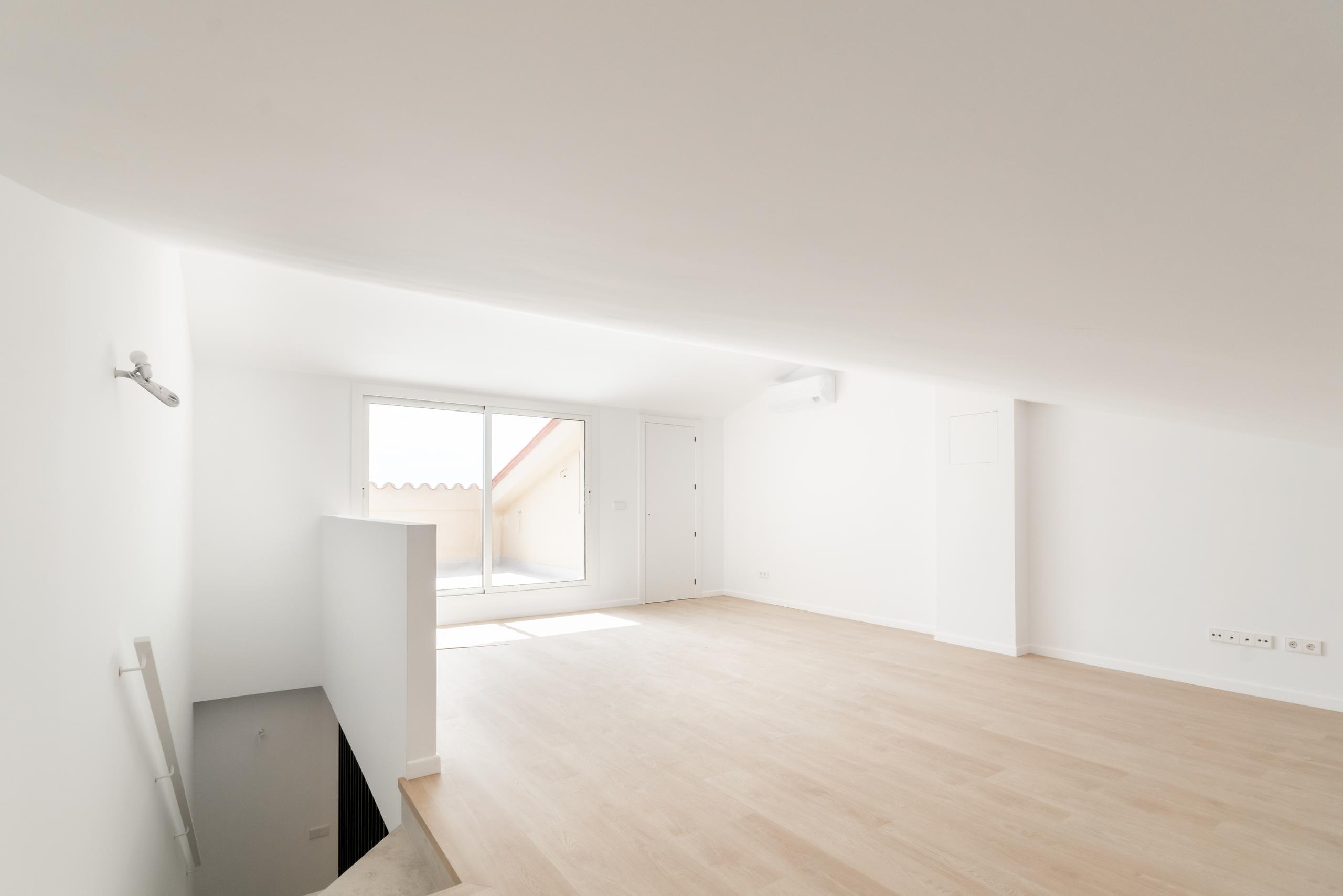 Espaciosa buhardilla con suelo de parquet claro, techo inclinado y salida a terraza exterior