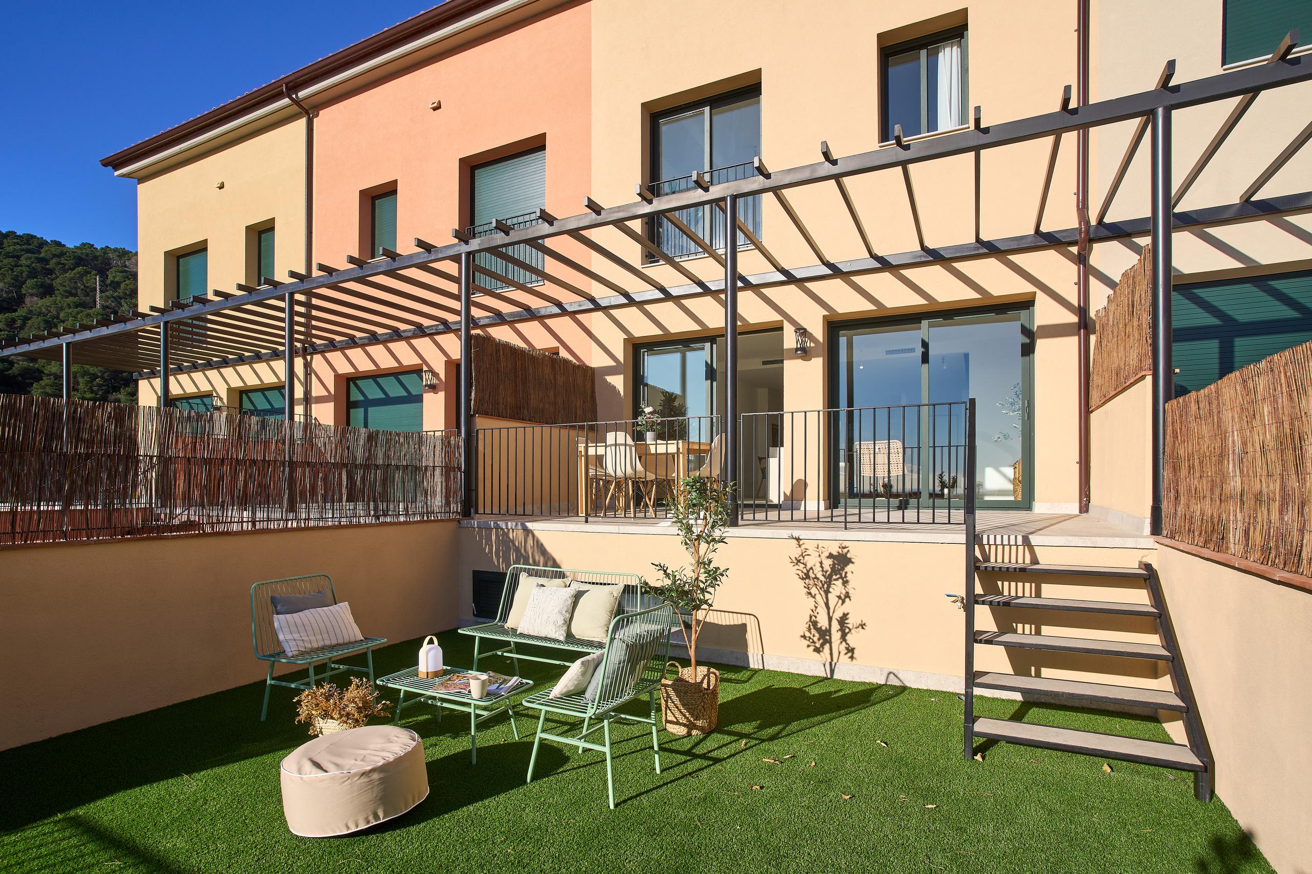 Fachada trasera de casa adosada con jardín privado, terraza elevada y pérgola de madera