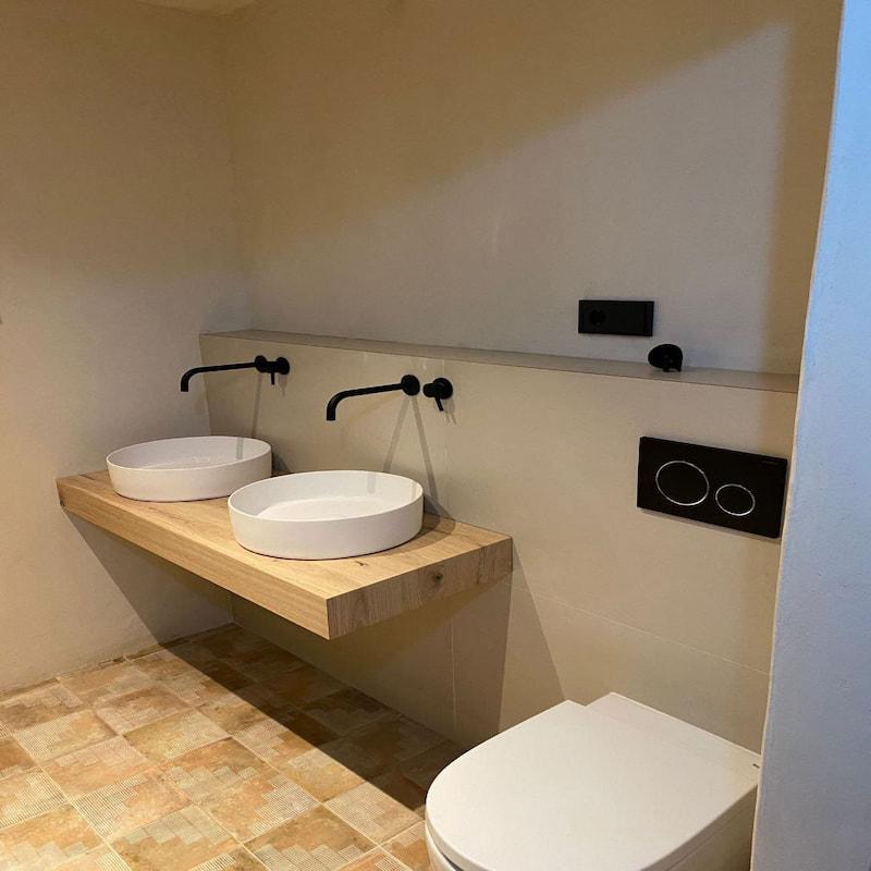 Baño rústico con tocador de madera y lavabos redondos en Ibiza.